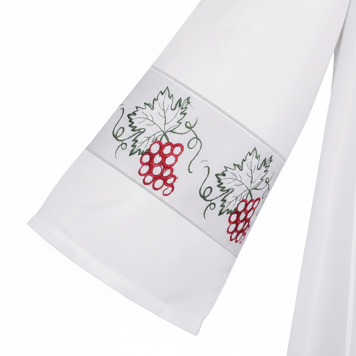 Close-up detail of white clergy alb robe sleeve cuff showing grape vine and red grape cluster embroidery band, white background