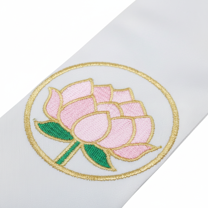 Close-up detail of white clergy stole showing pink lotus flower embroidery inside gold circle ring with white fringe tassels, white background