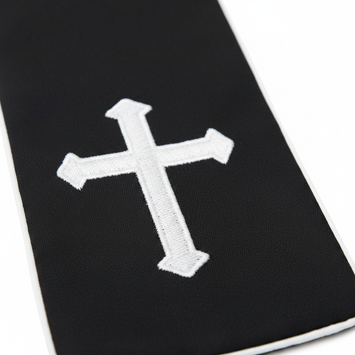 Close-up detail of black clergy stole end panel showing white embroidered Latin cross and white piping border, white background