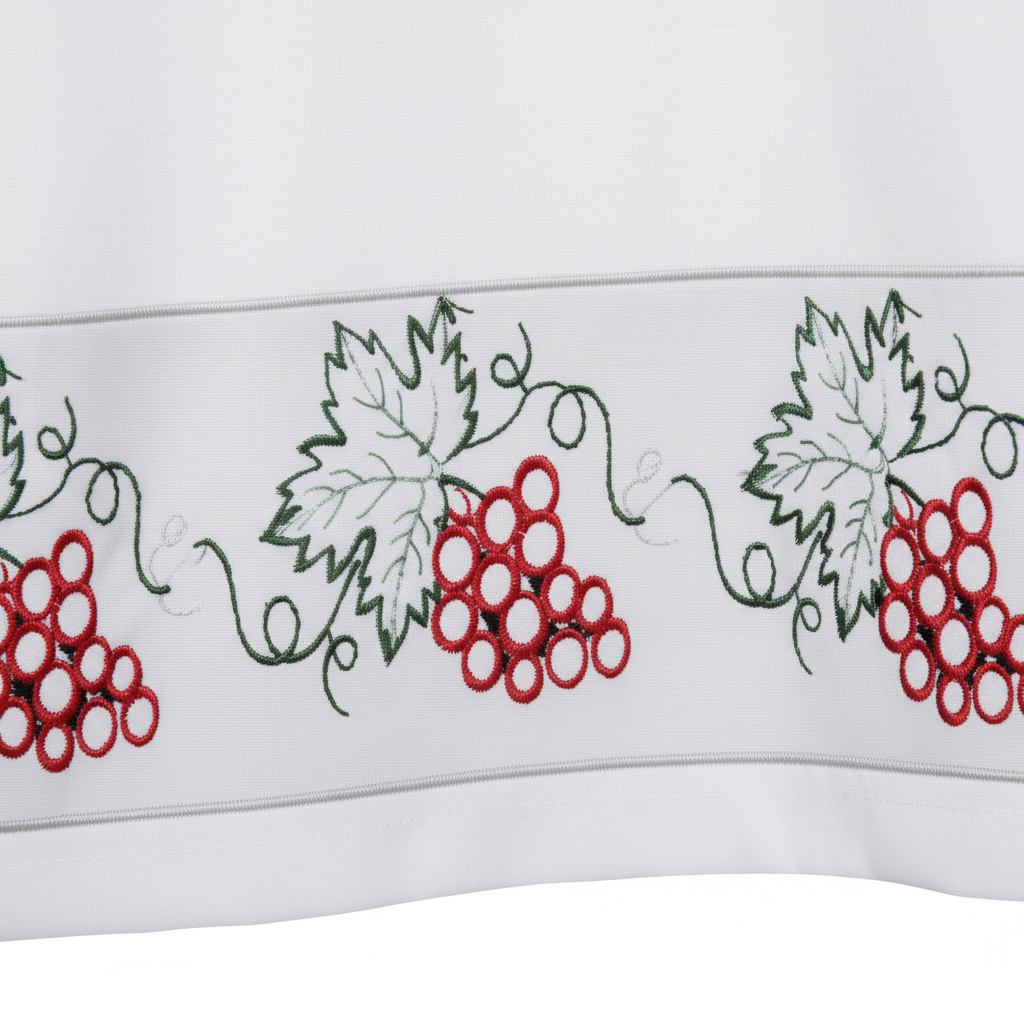 Close-up detail of white clergy alb robe hem showing grape vine and red grape cluster embroidery band, white background