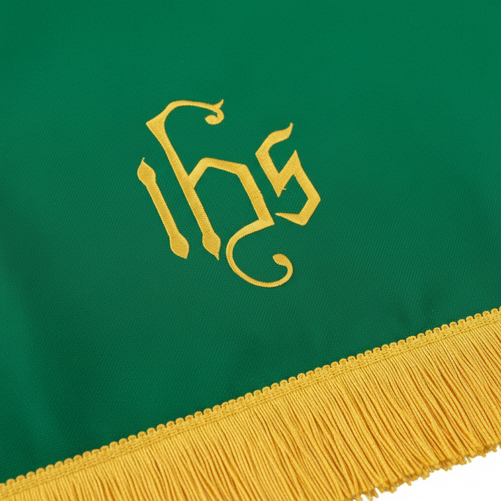 Close-up detail of green liturgical pulpit stole showing embroidered gold IHS monogram and gold fringe tassel, white background
