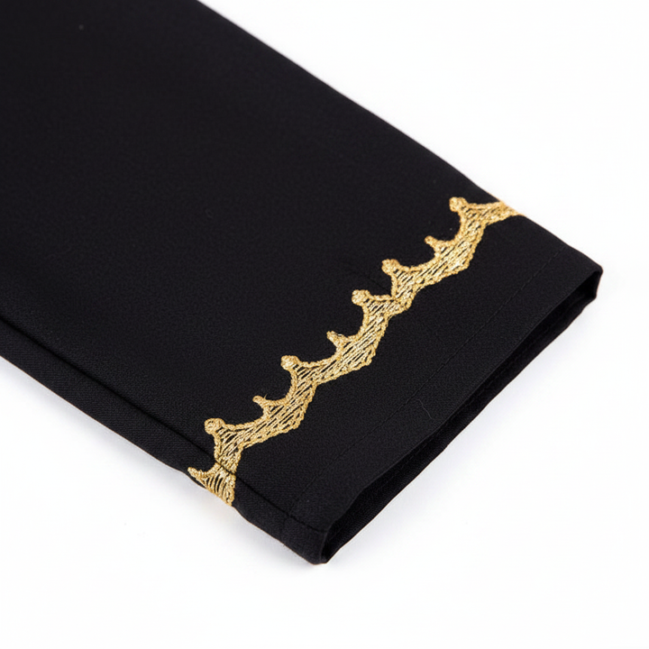 Close-up detail of black thobe sleeve cuff showing ornate gold embroidery trim band at wrist, white background