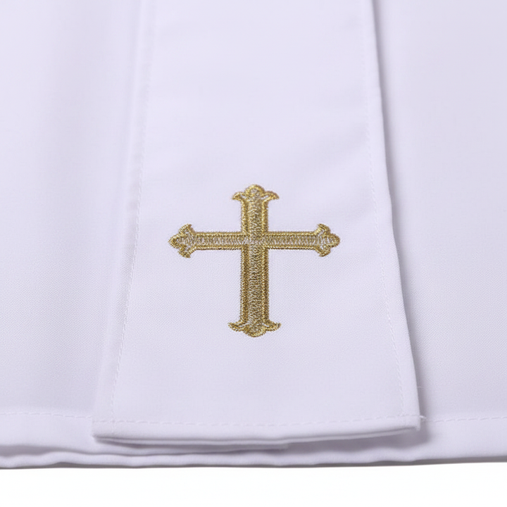 Close-up detail of white cassock robe lower hem showing gold cross embroidery on white fabric, white background