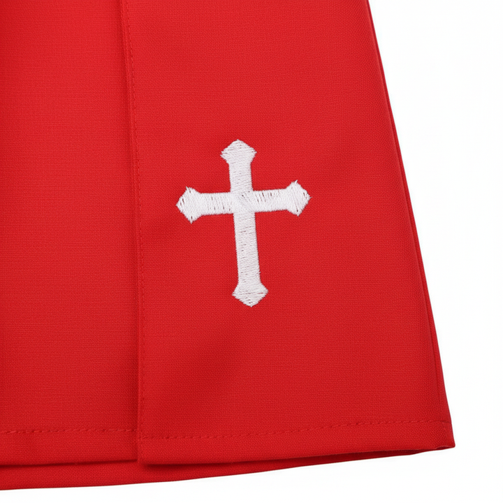 Close-up detail of red cassock robe lower hem showing white cross embroidery on red fabric, white background